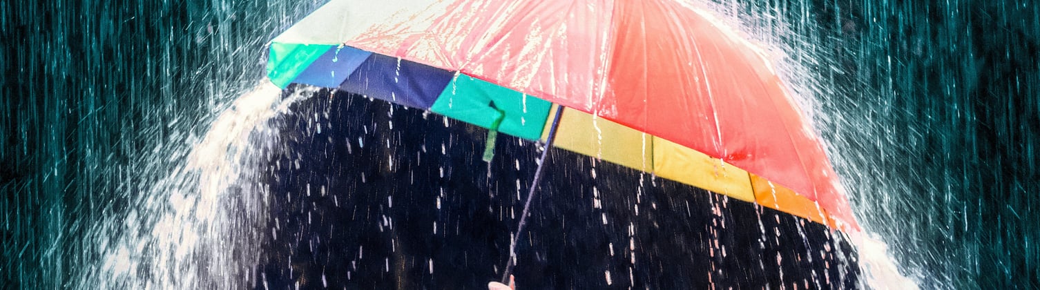 A colorful umbrella open, being rained on by heavy rain with a dark background.
