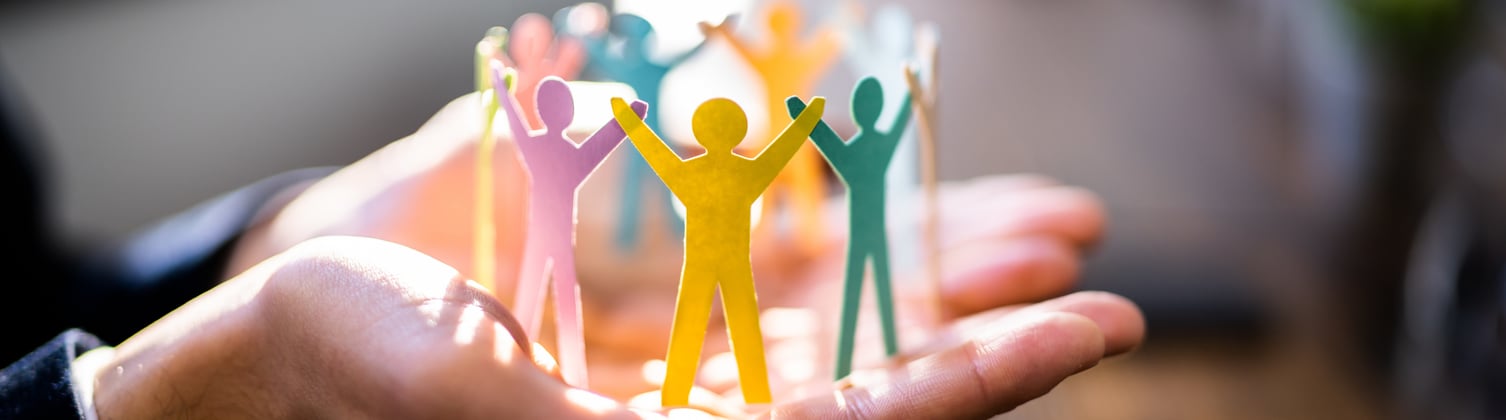 A person with their hand palm side up holding up a colorful paper chain of people cutout holding raised hands.