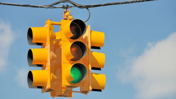 Yellow traffic light hanging from a cable with a blue sky backdrop.