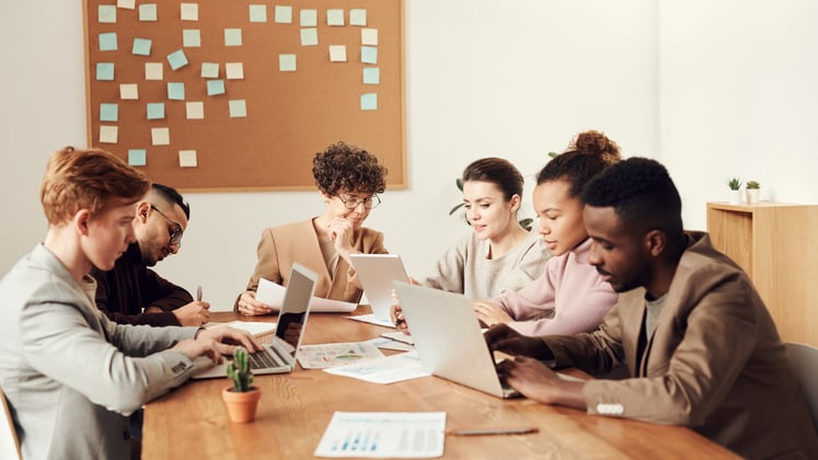 A group of people with their laptops sitting on a boardroom table in a meeting room.