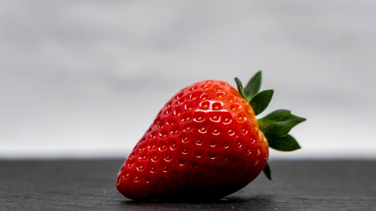 A single strawberry placed on a dark grey surface.