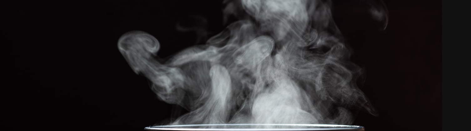 A black cup with a lot of steam coming out of it, set in a black background.