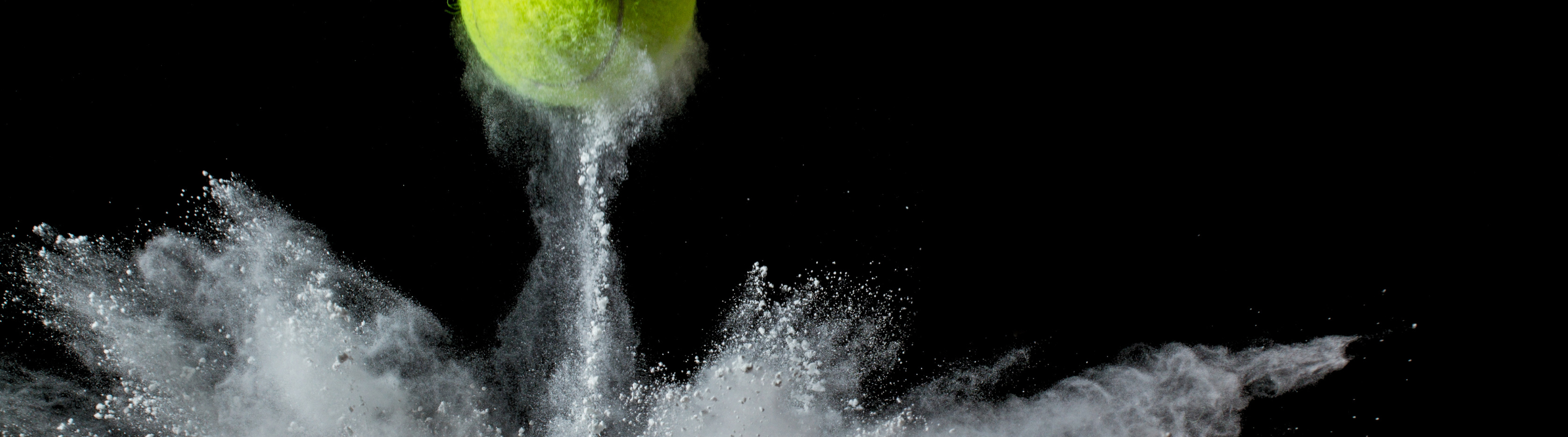 A tennis ball bouncing off a surface with a white powder explosion in a black backdrop.