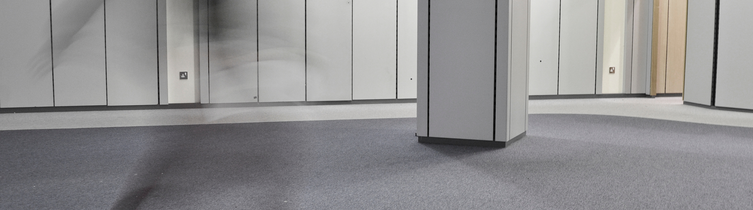 A shadow figure of a man in a motion blur going through a grey room.