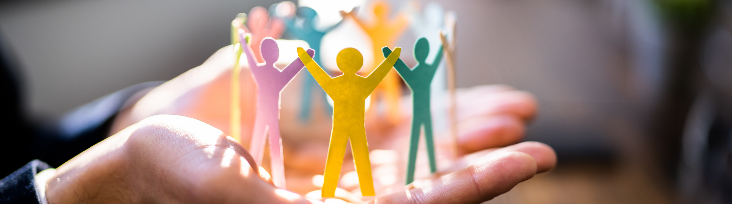A person with their hand palm side up holding up a colorful paper chain of people cutout holding raised hands.