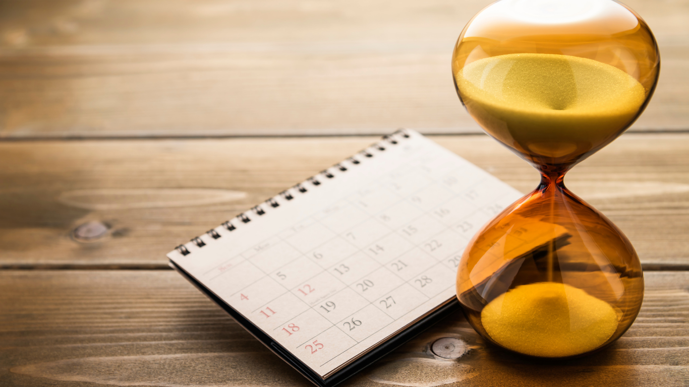 Hourglass with sand dropping to the bottom, placed next to a calendar.