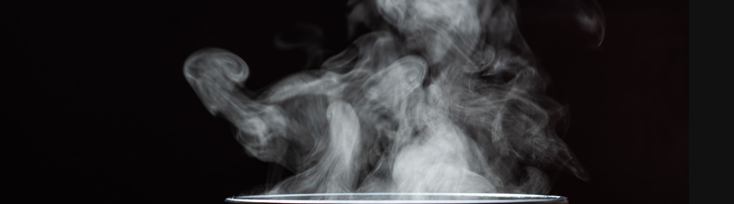 A black cup with a lot of steam coming out of it, set in a black background.