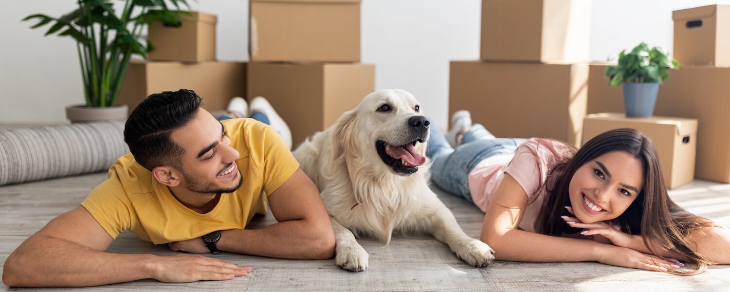 Young diverse couple lying on floor among carton boxes with their cute dog