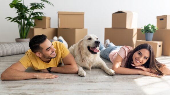 Young diverse couple lying on floor among carton boxes with their cute dog